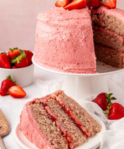 slice of strawberry layer cake on a plate with the whole cake in the background
