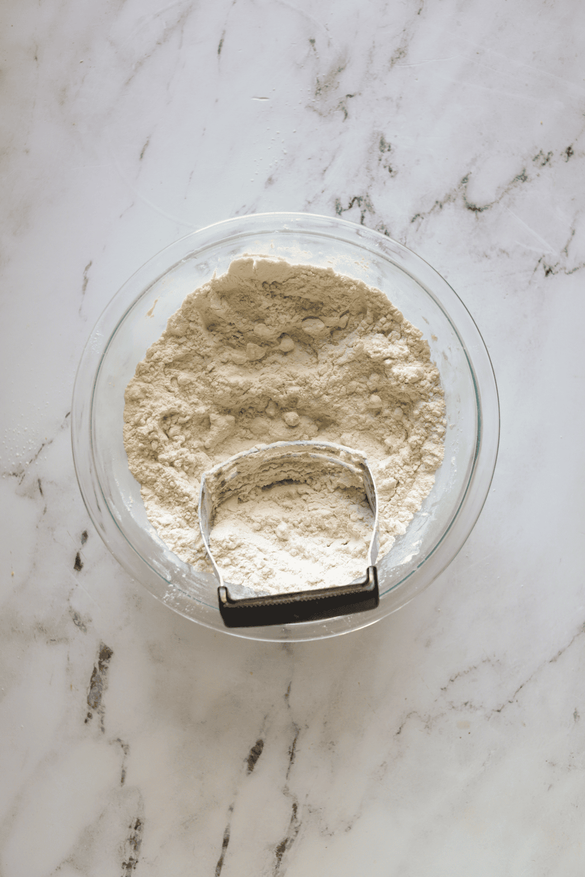 glass bowl of biscuit mixture with butter cut in, and pastry cutter in bowl