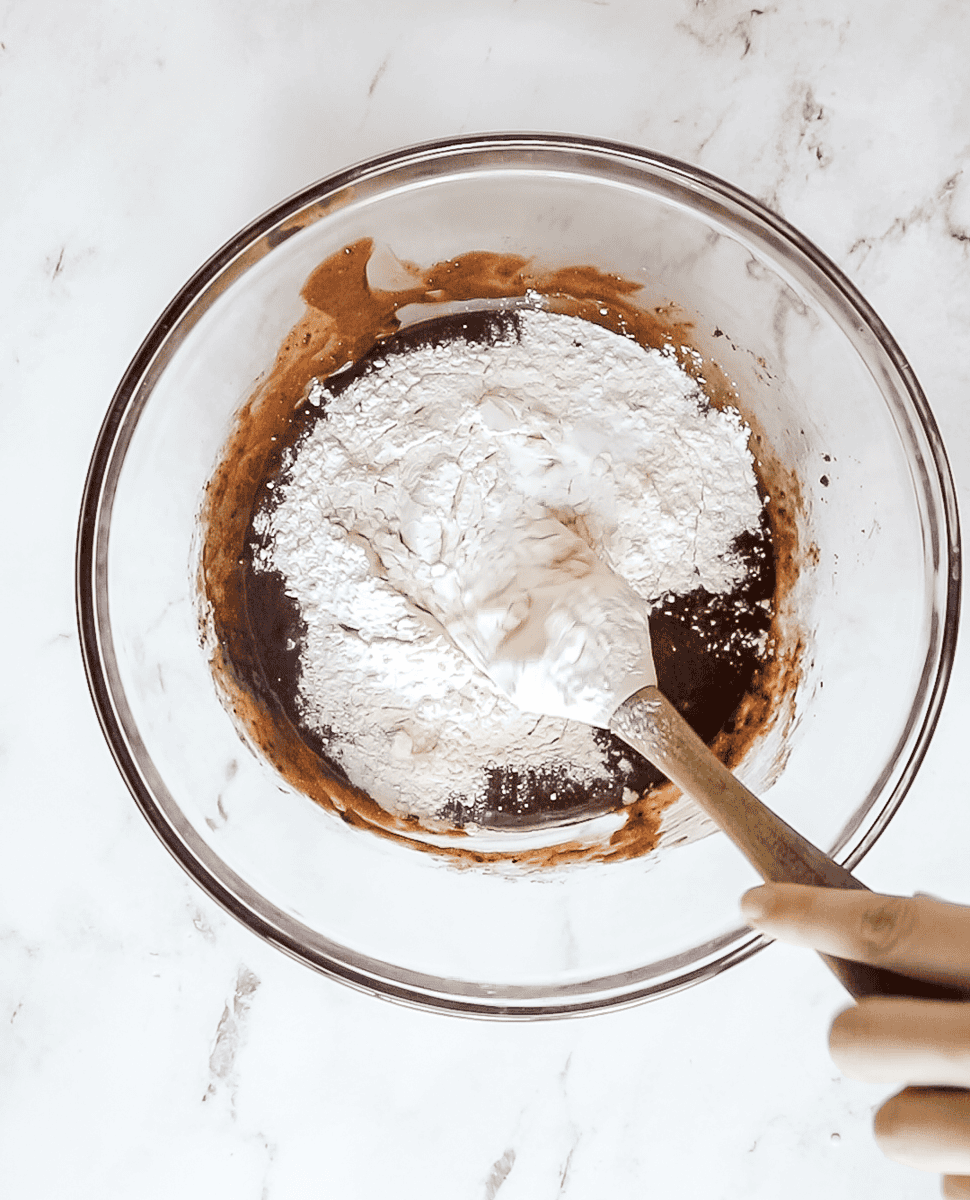 dry ingredients (all purpose flour, baking powder, and salt) being stirred into chocolate cookie dough with a spatula
