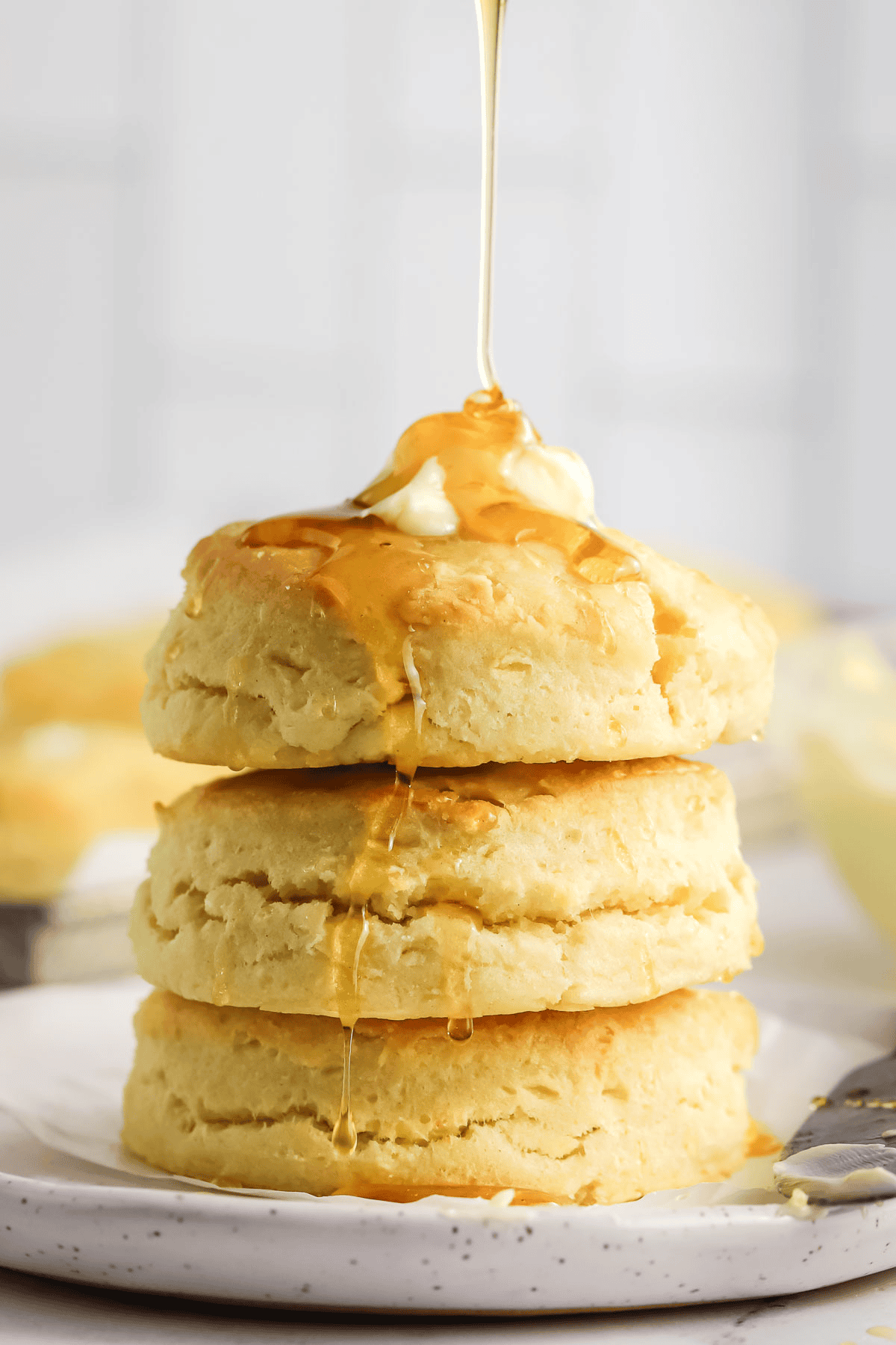 three cream biscuits stacked on a plate topped with butter and drizzled with honey