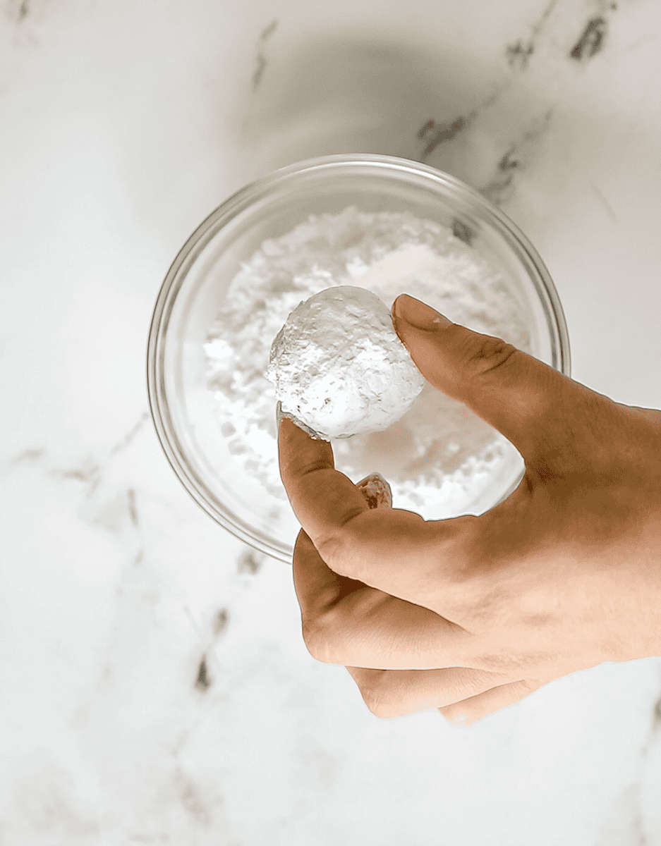 cookie dough ball being rolled in powdered sugar