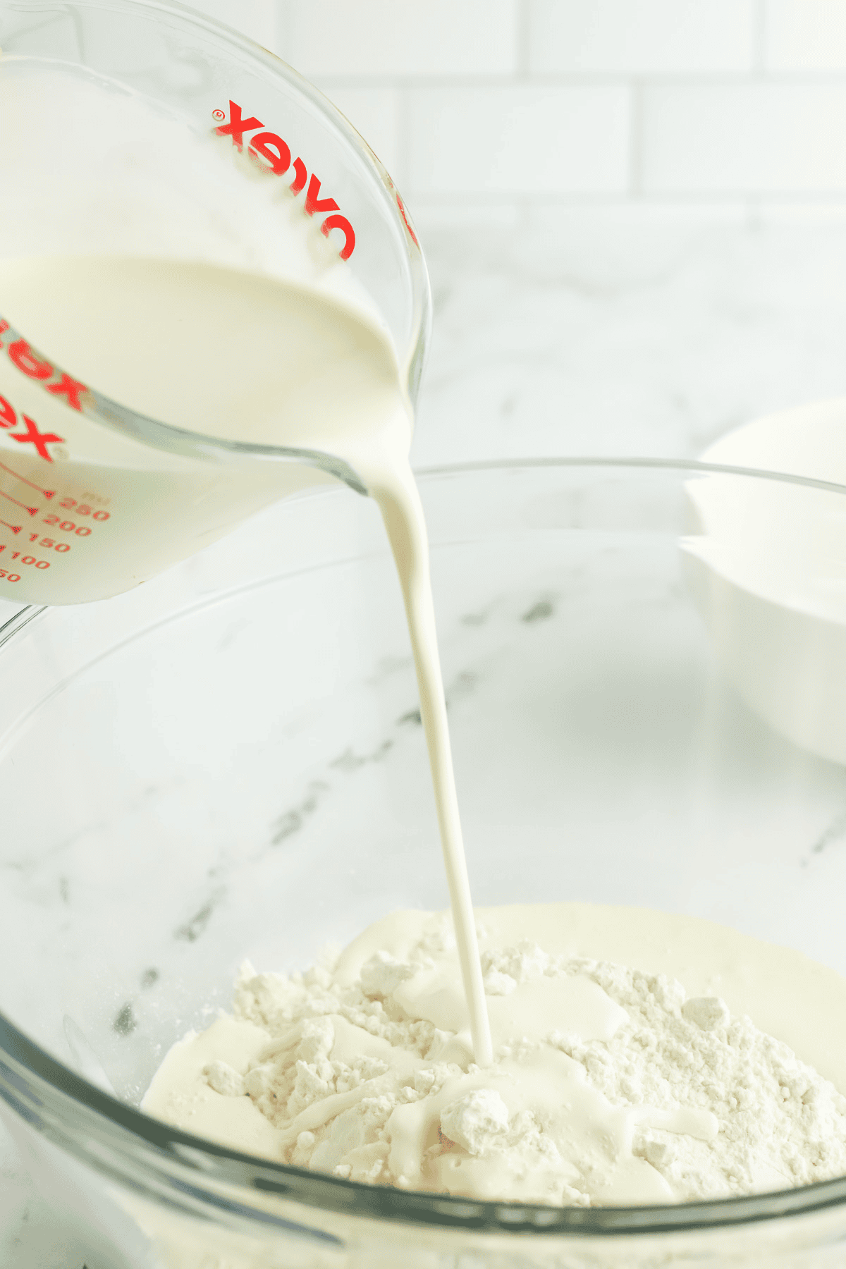 heavy cream being poured into a bowl of self rising flour