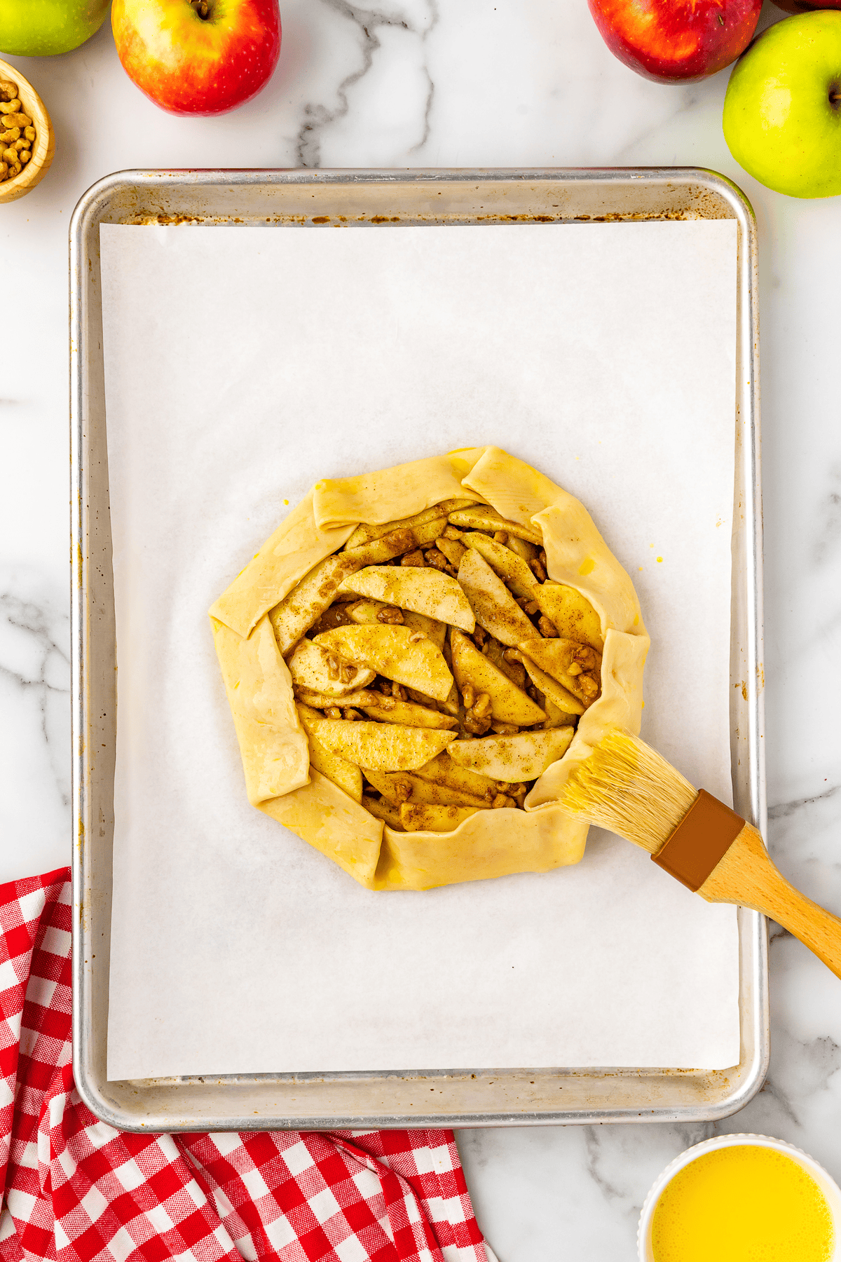pastry brush brushing on egg wash onto unbaked apple crostata pie dough