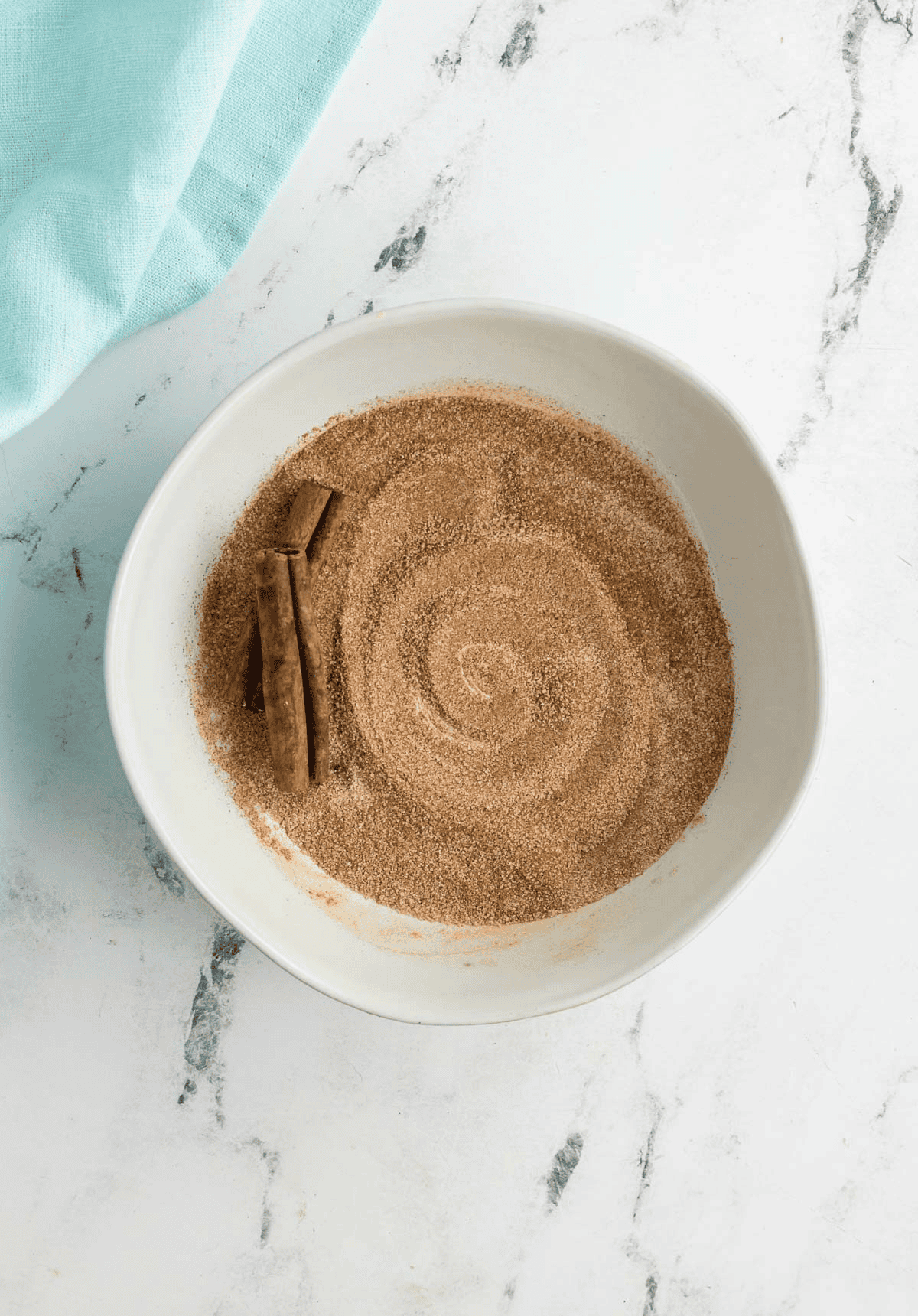 bowl of cinnamon sugar with two cinnamon sticks in it