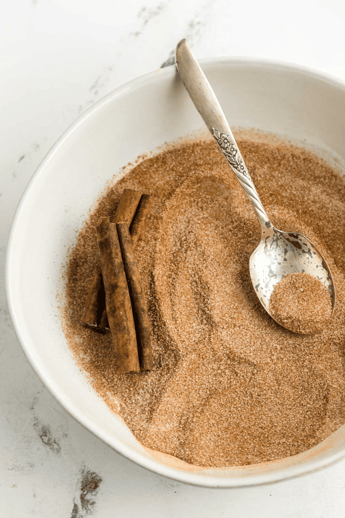 bowl of cinnamon sugar with cinnamon sticks and a spoon in it