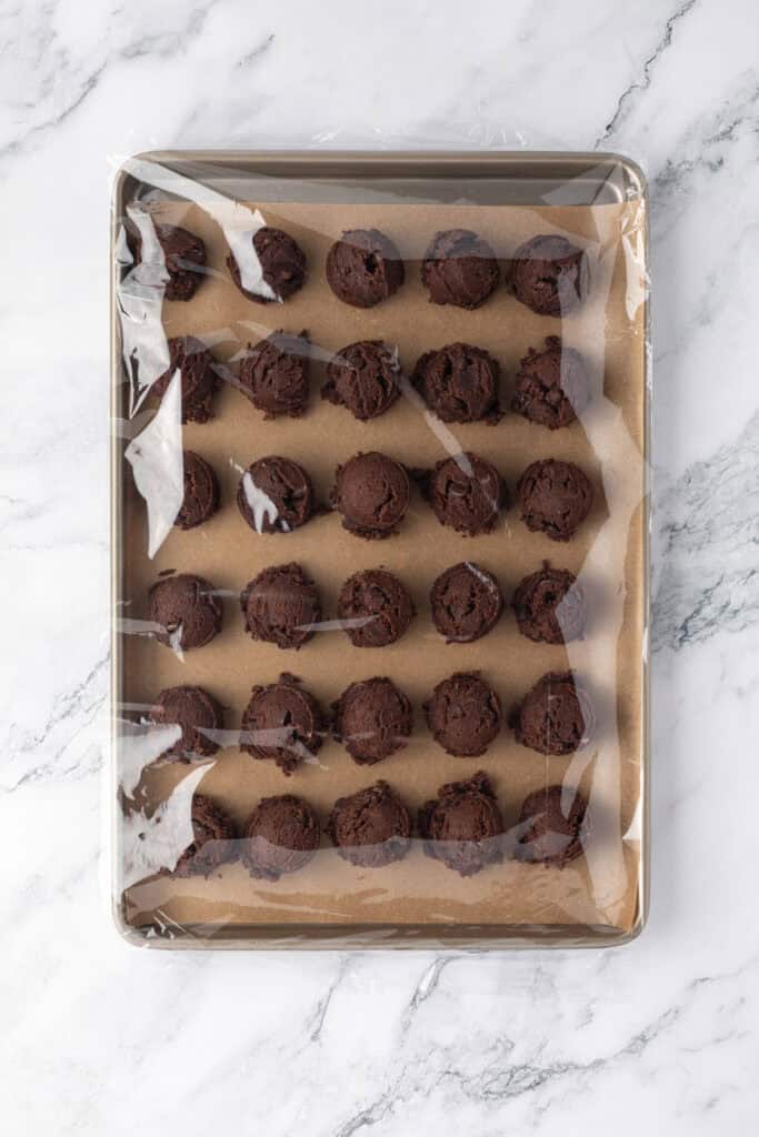cookie dough balls on cookie sheet wrapped in cookie sheet